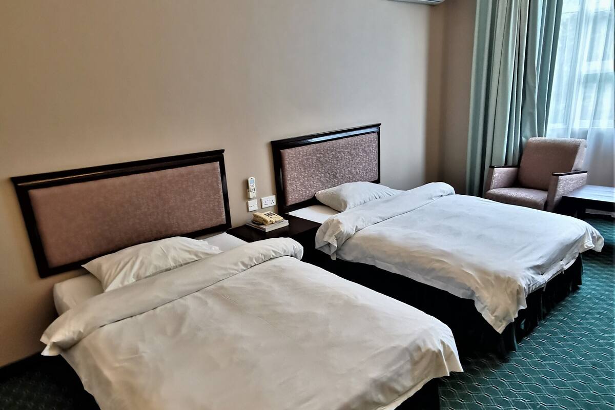 Ein Hotelzimmer mit zwei Betten, einem Sessel, einer Klimaanlage und einem Vorhangfenster.