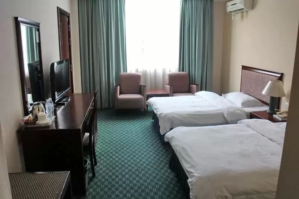 Une chambre d’hôtel avec deux lits, un bureau avec une chaise, une télévision et une fenêtre avec des rideaux.