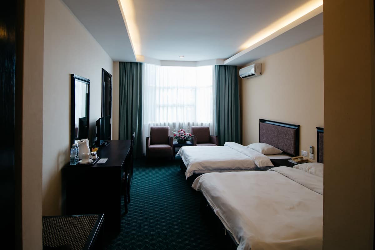 Ein Hotelzimmer mit zwei Betten, einem Schreibtisch, einem Stuhl und einem großen Fenster mit Vorhängen.