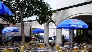 An outdoor cafe with yellow chairs and tables, blue umbrellas, and potted plants. - Traders Inn (Bandar Seri Begawan)
