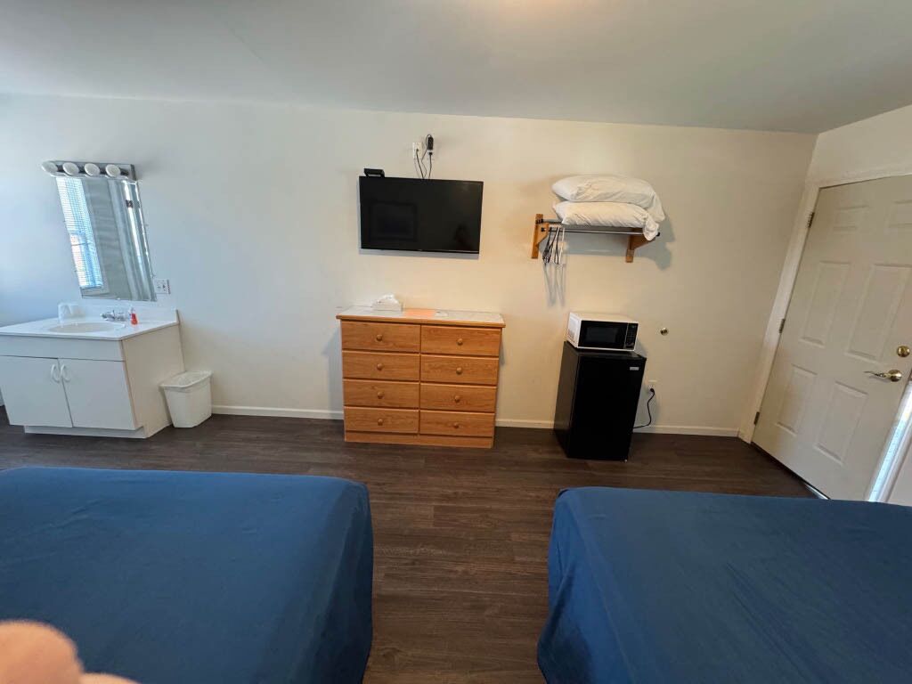 Una habitación con dos camas, un aparador de madera, un televisor, un microondas y una puerta.