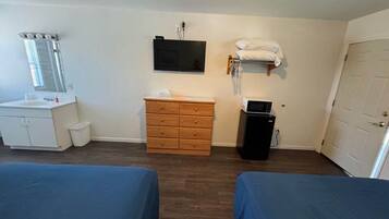 Una habitación con dos camas, un aparador de madera, un televisor, un microondas y una puerta.