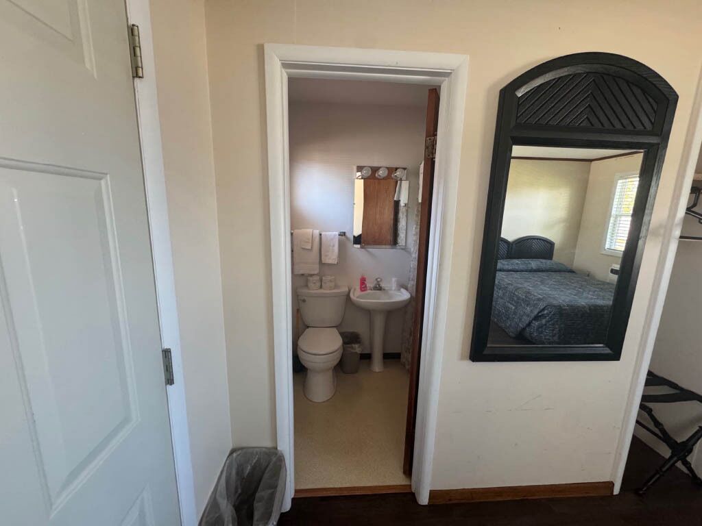 Een kleine kamer met een deur naar een badkamer, waar een toilet, wastafel en spiegel staan.