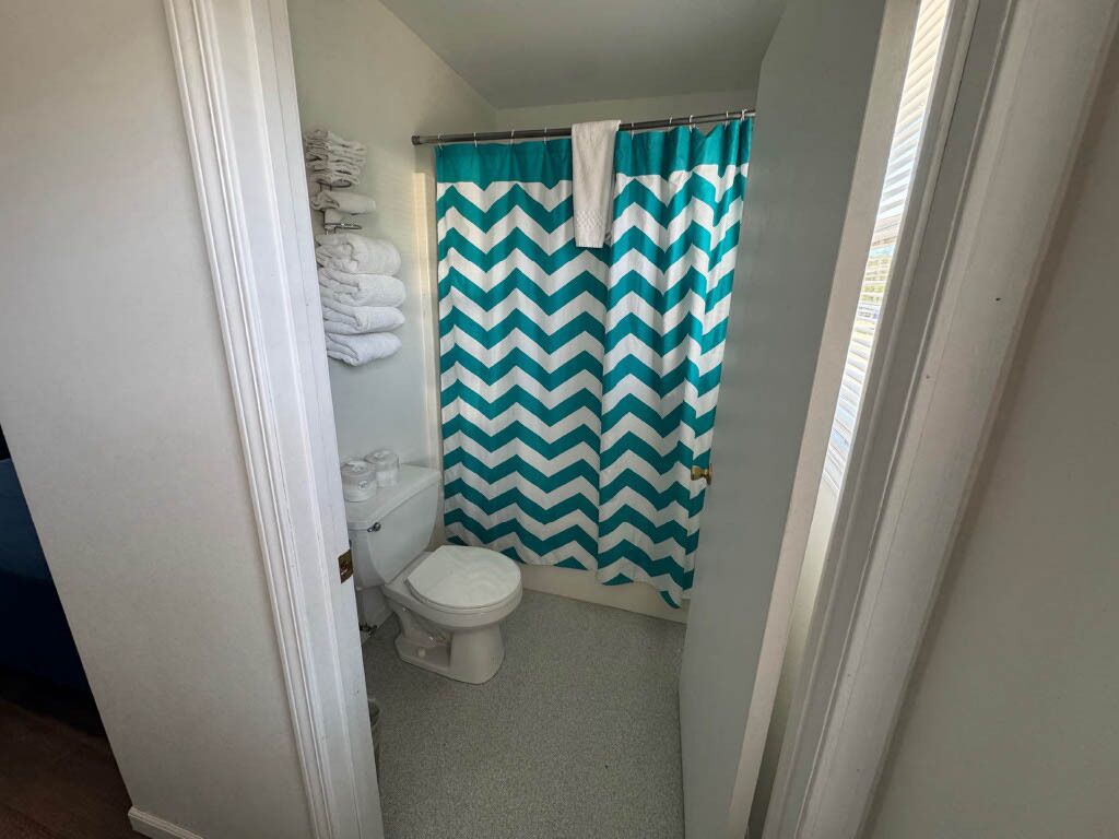A small bathroom with a toilet, a shower curtain with a chevron pattern, and a towel rack with folded towels.