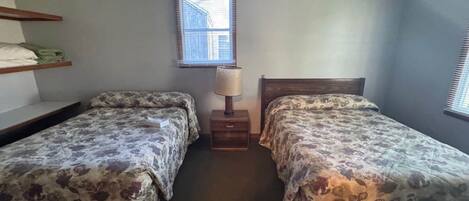 A bedroom with two beds, a nightstand, a lamp, and a window.