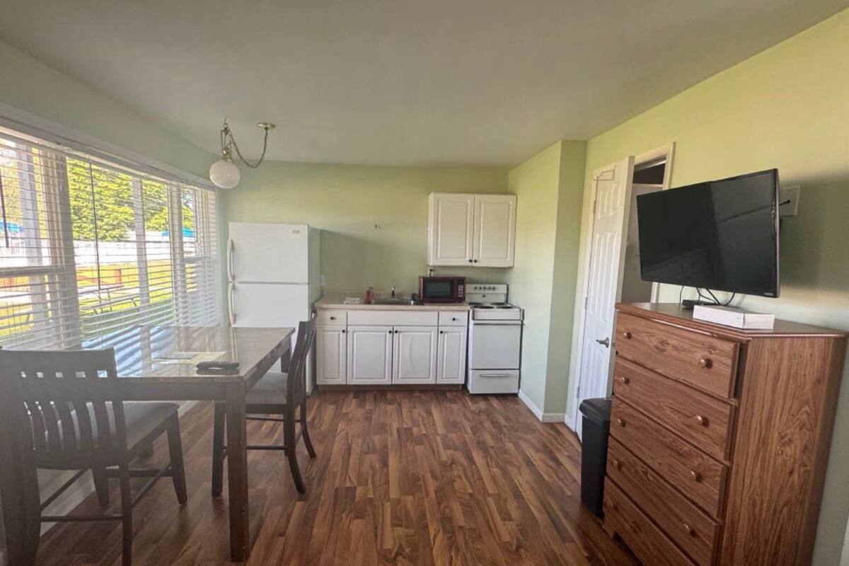 Une cuisine compacte avec des meubles blancs, une table à manger en bois et un téléviseur posé sur une commode.