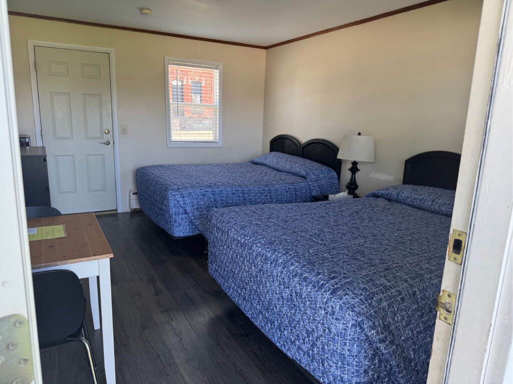 Ein Zimmer mit zwei Betten, einem Schreibtisch und einem Fenster mit Jalousien.