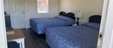 A room with two beds, a desk, and a window with blinds.