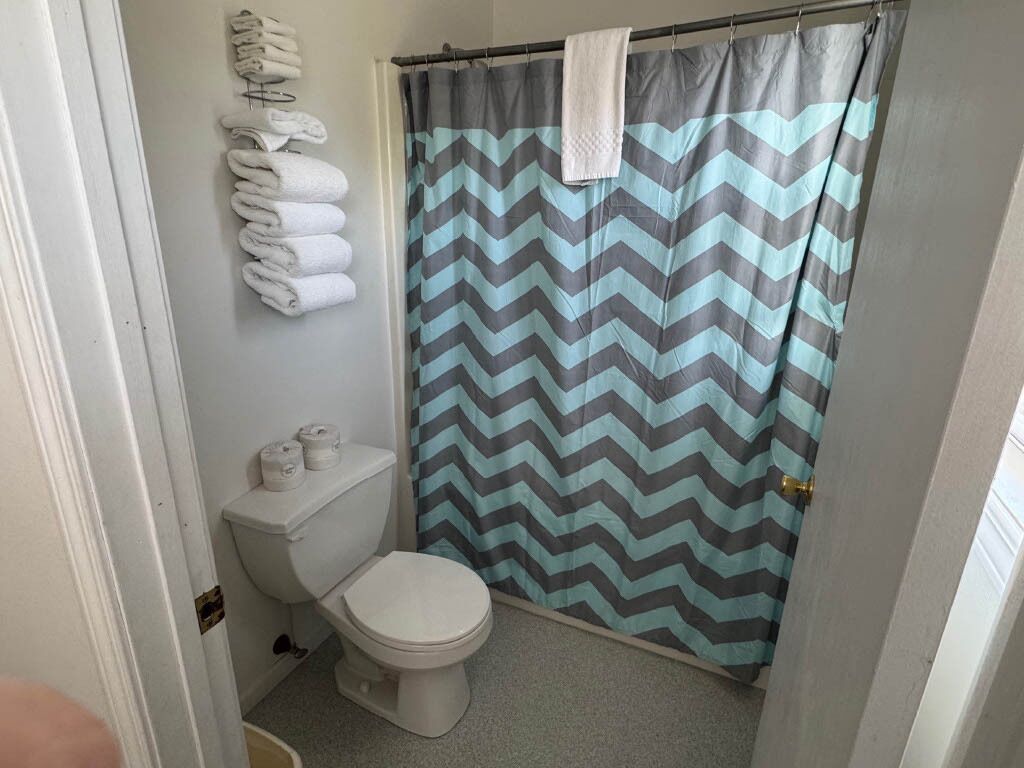 Un baño con inodoro, cortina de ducha y toallas colgadas en la pared.