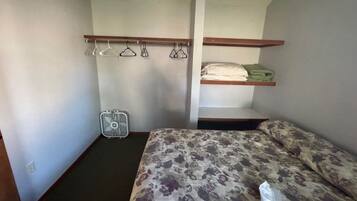 Habitación pequeña con una cama, un ventilador y un estante con ropa doblada.