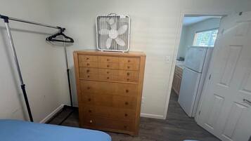 Un dormitorio con dos camas, un aparador de madera, un perchero y un ventilador de techo.