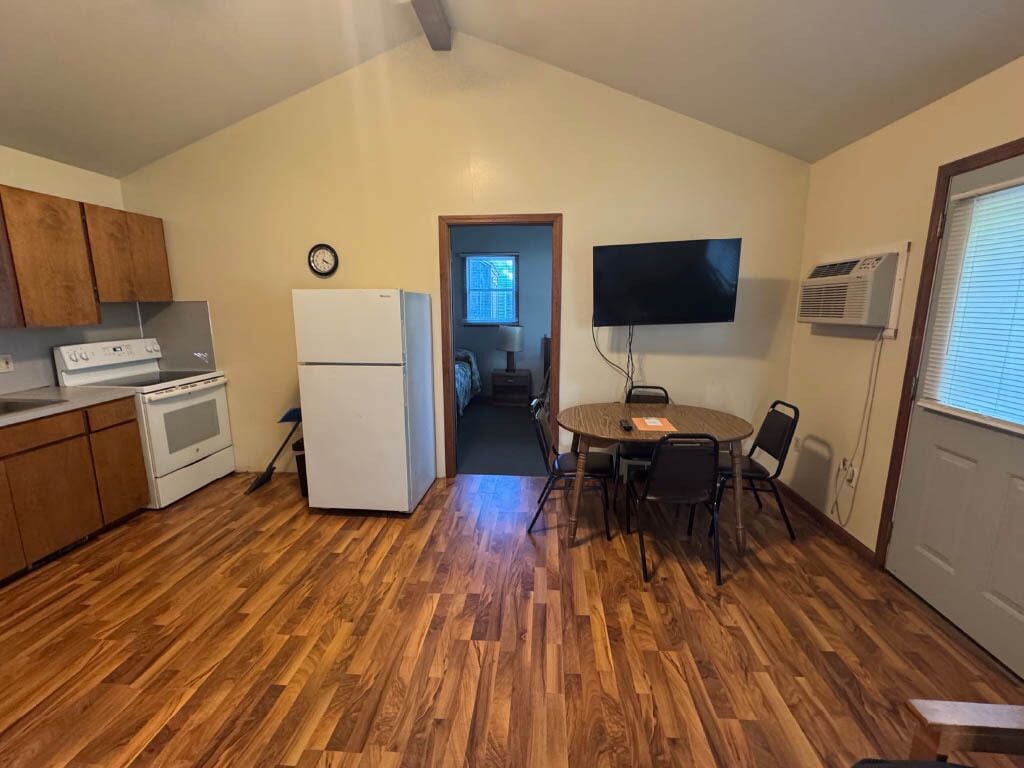 A compact kitchen with wooden cabinets, a refrigerator, and a dining area with a table and chairs.