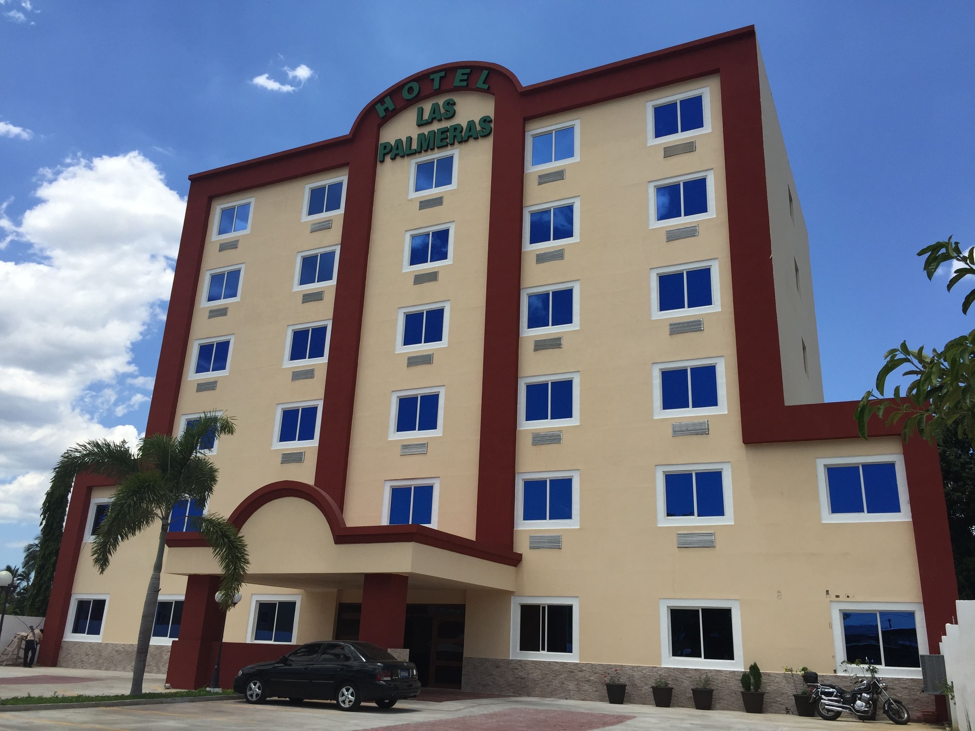 A hotel building with multiple floors, a red and beige facade, and a sign that reads "HOTEL LAS PALMERAS".