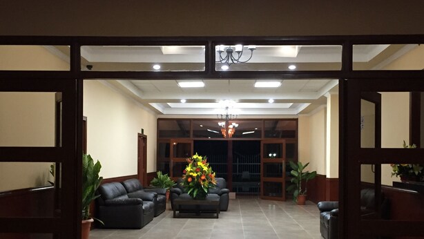 A lobby with a reception desk, two sofas, a chandelier, and potted plants. - Hotel Las Palmeras (Sonzacate)