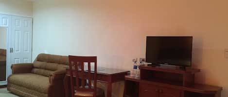 A living room with a sofa, a wooden chair, a TV on a wooden stand, and a cabinet.