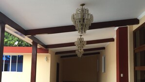 A spacious corridor with a chandelier, tiled floor, and a trash bin. - Hotel Las Palmeras (Sonzacate)
