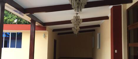 A spacious corridor with a chandelier, tiled floor, and a trash bin.