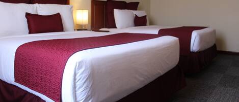 A hotel room with two beds, each with white linens and red bedding. There is a nightstand with a lamp between the beds.