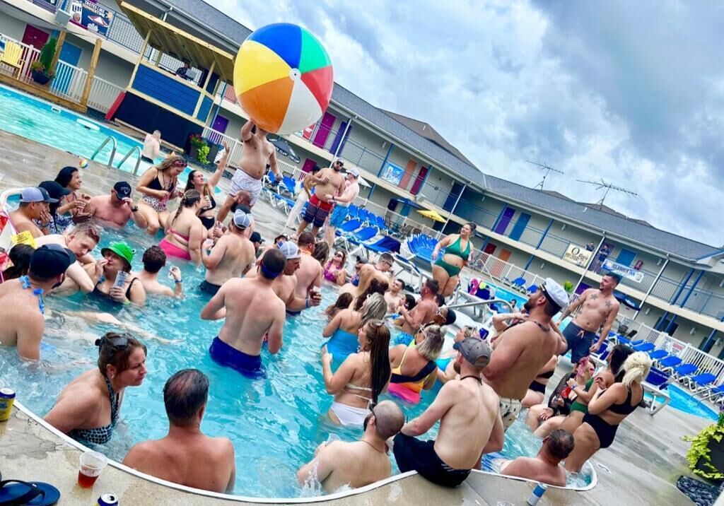 Zona de piscina con varias personas, algunas nadando y otras junto a la piscina.
