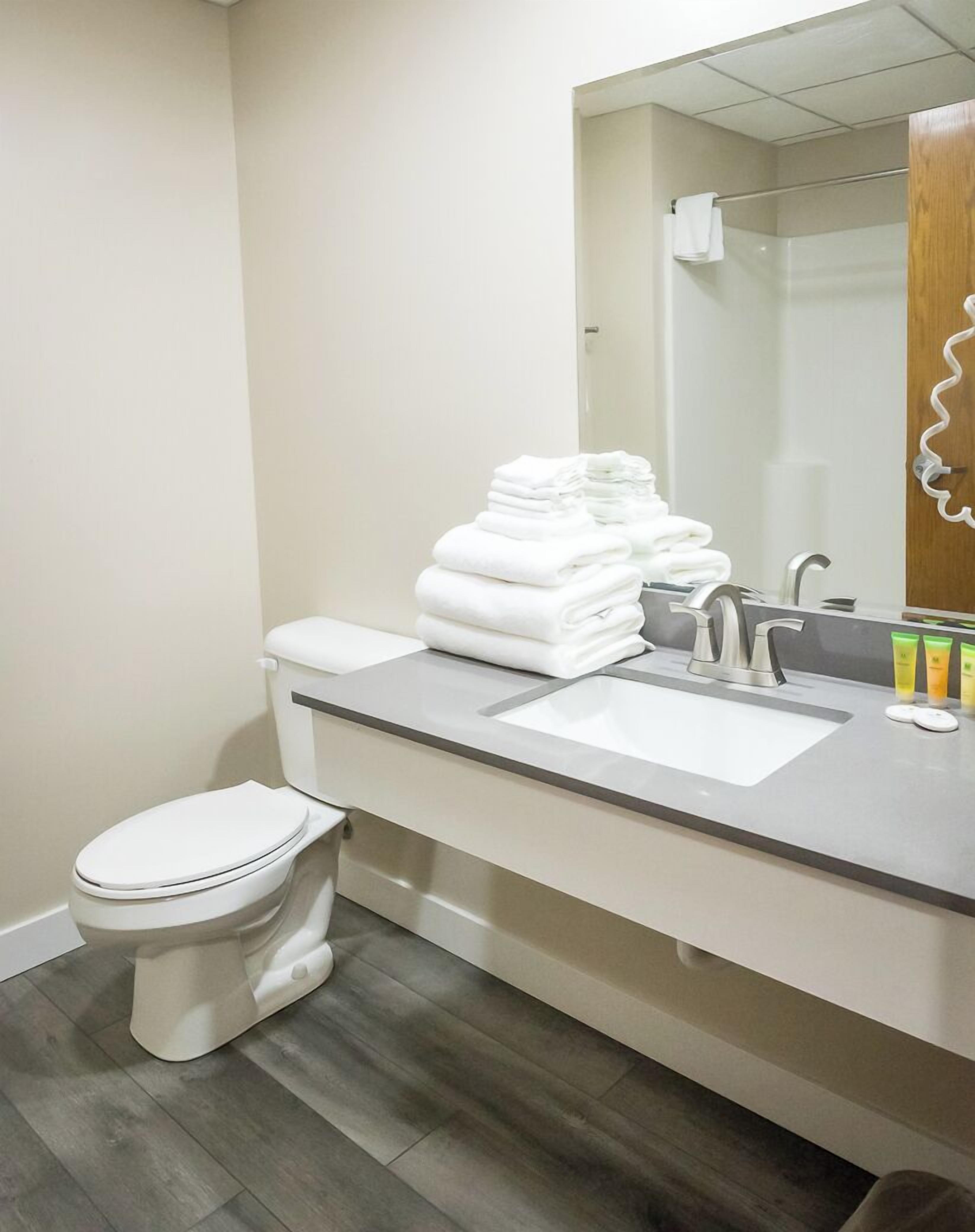 Een moderne badkamer met een toilet, een wastafel met spiegel en een stapel witte handdoeken.