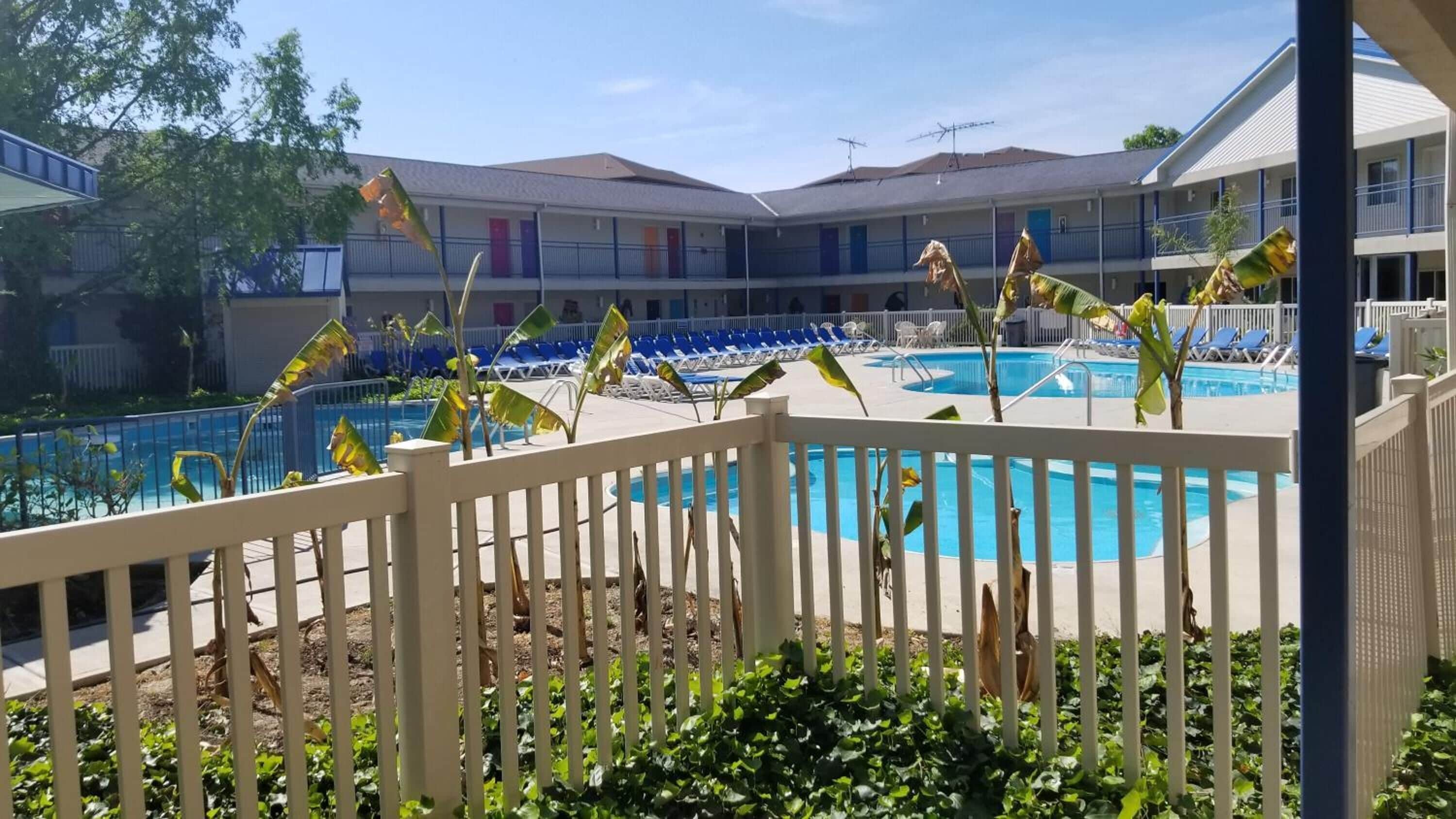 A pool area with a white fence, lounge chairs, and a building with multiple balconies in the background.