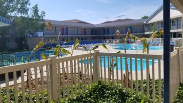 Area piscina con recinzione bianca, lettini e un edificio sullo sfondo con numerosi balconi.