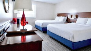 Ein Hotelzimmer mit zwei Betten, einem Schreibtisch, einer Lampe und einem Fenster.