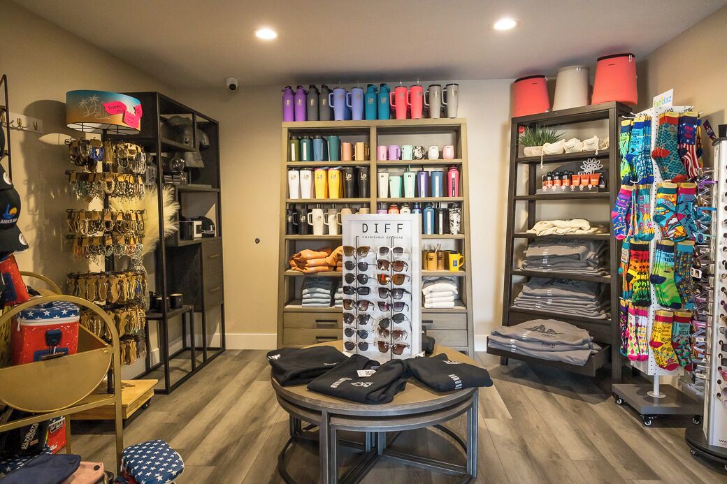 A retail store with shelves of colorful water bottles, a rack of sunglasses, and racks of socks and t-shirts.