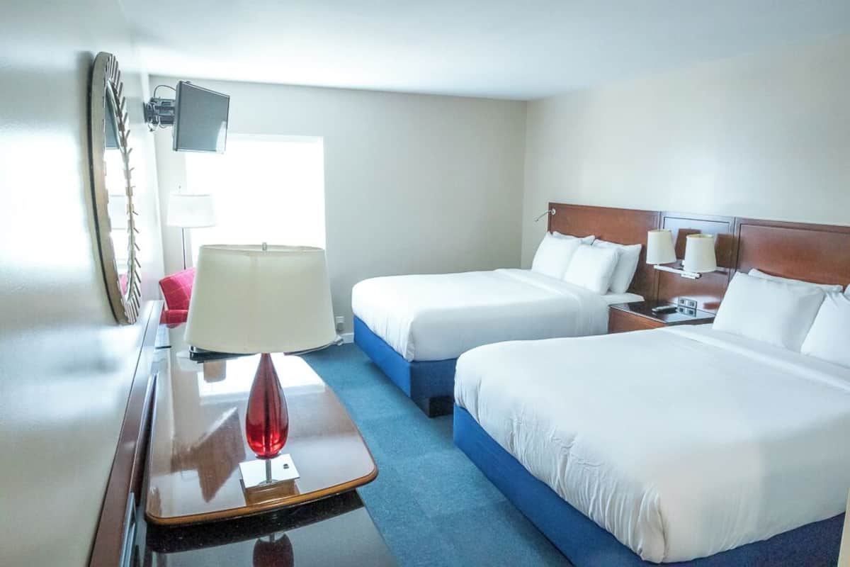 A hotel room with two beds, a desk with a lamp, a TV, and a window.