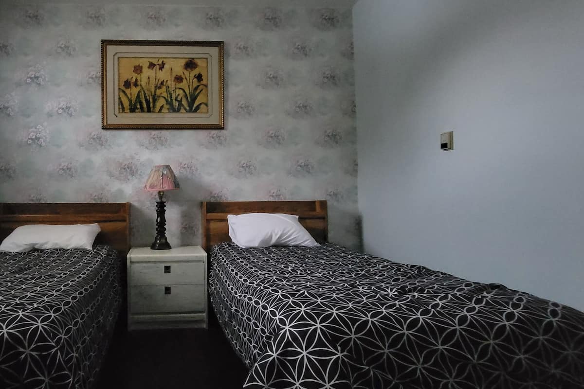 A room with two beds, a nightstand, a lamp, and a floral-patterned wall.