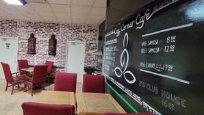 A cafe with red chairs and tables, a menu on the wall, and a brick wall with a painting. - Cosmopolitan Hotel (Blairmore)