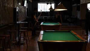 A pool table with a green felt surface, surrounded by wooden stools. - Cosmopolitan Hotel (Blairmore)