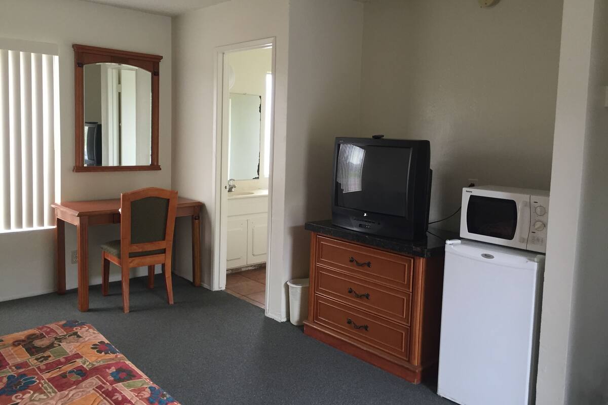 A hotel room with a desk, chair, television, microwave, and a bed with a colorful bedspread.