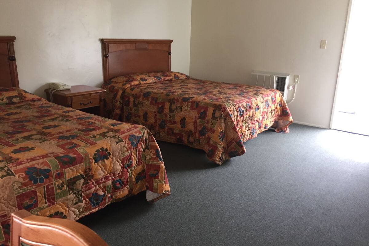 A room with two single beds, a wooden nightstand, a desk, and a radiator.