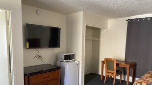 Una camera compatta con un letto, una scrivania con una sedia, un forno a microonde, un frigorifero, una TV a parete e un armadio.
