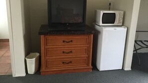 Angolo cottura con televisione su un mobile in legno, forno a microonde e frigorifero.