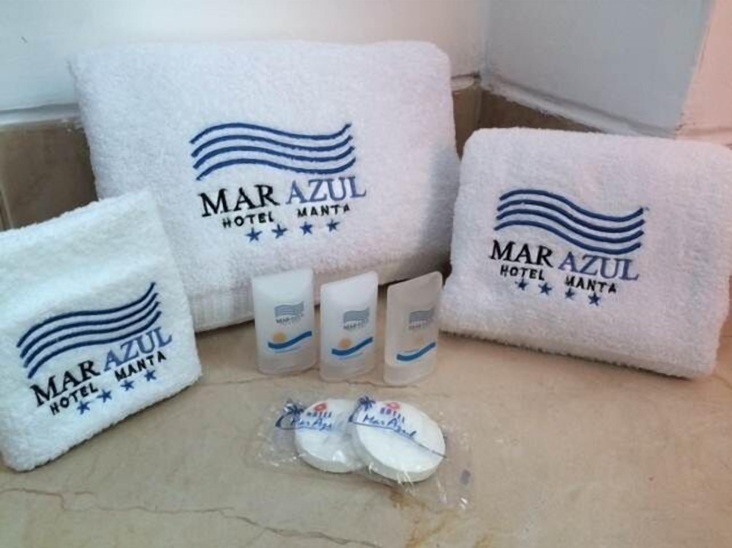 A set of white towels and toiletries with the Mar Azul Hotel Manta logo, indicating amenities provided to guests.