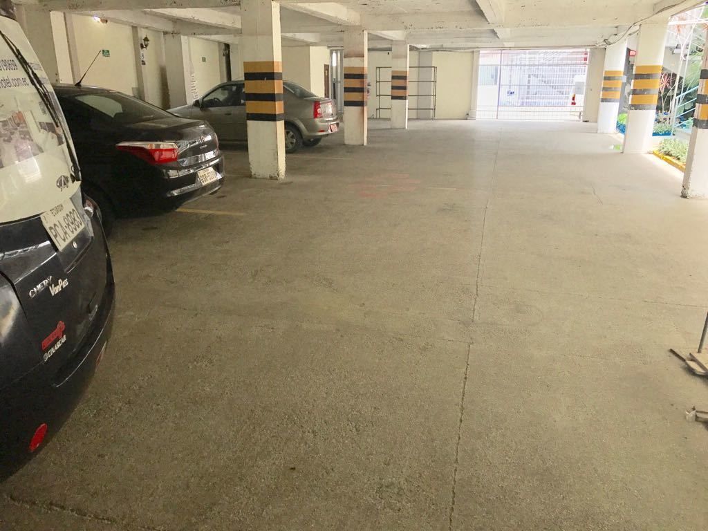 Un parking avec des planchers et des piliers en béton, caractérisé par des piliers rayés et quelques voitures garées.