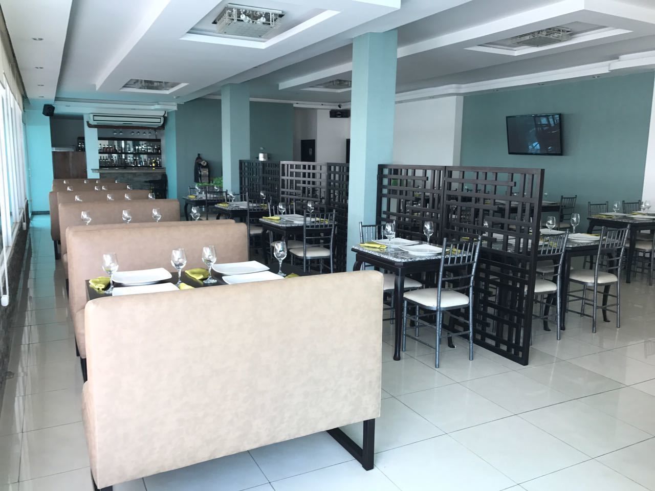Un restaurante moderno con cabinas y mesas, una zona de bar y un televisor en la pared.