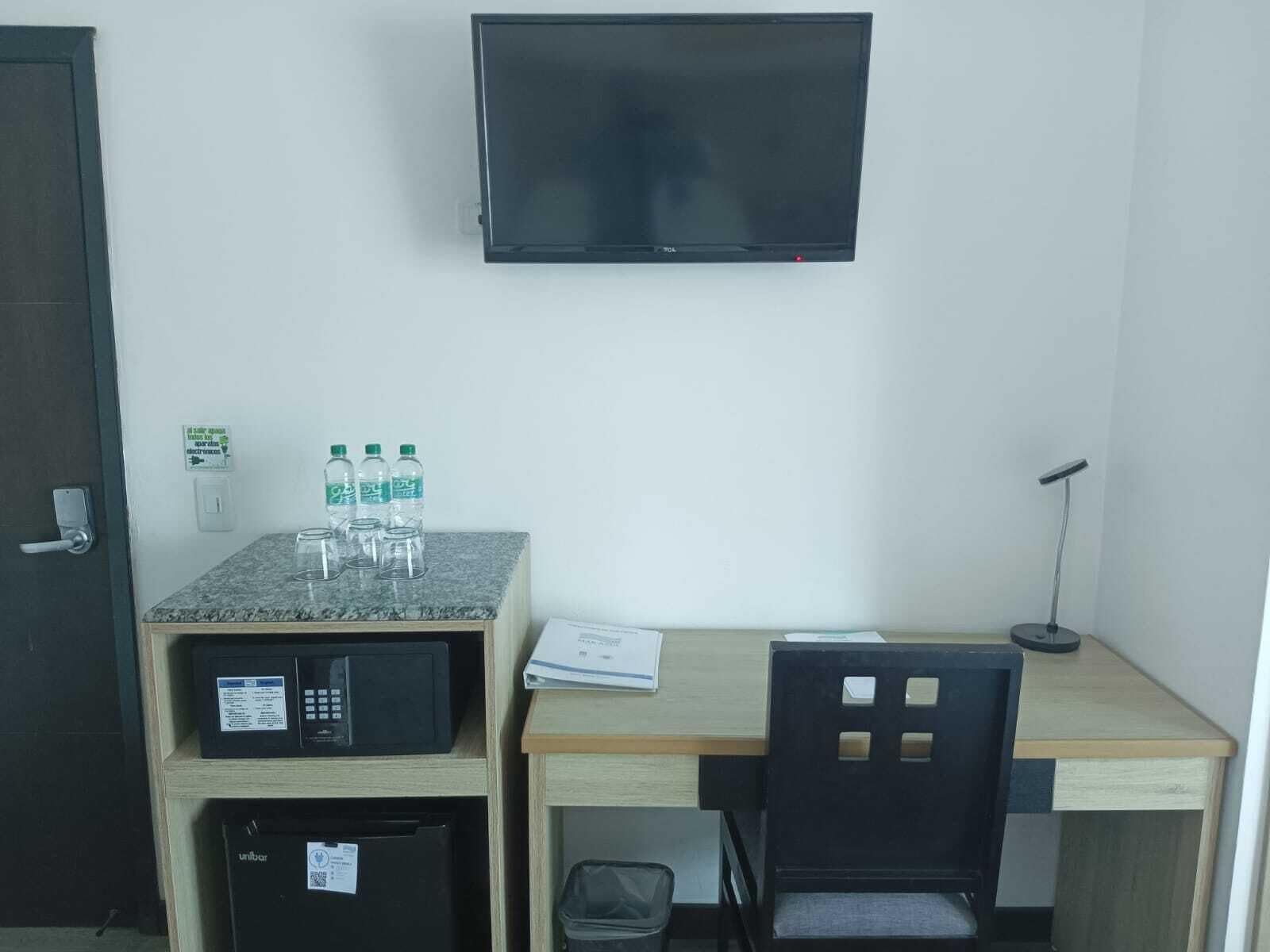 A small office space with a desk, chair, microwave, and a TV mounted on the wall.