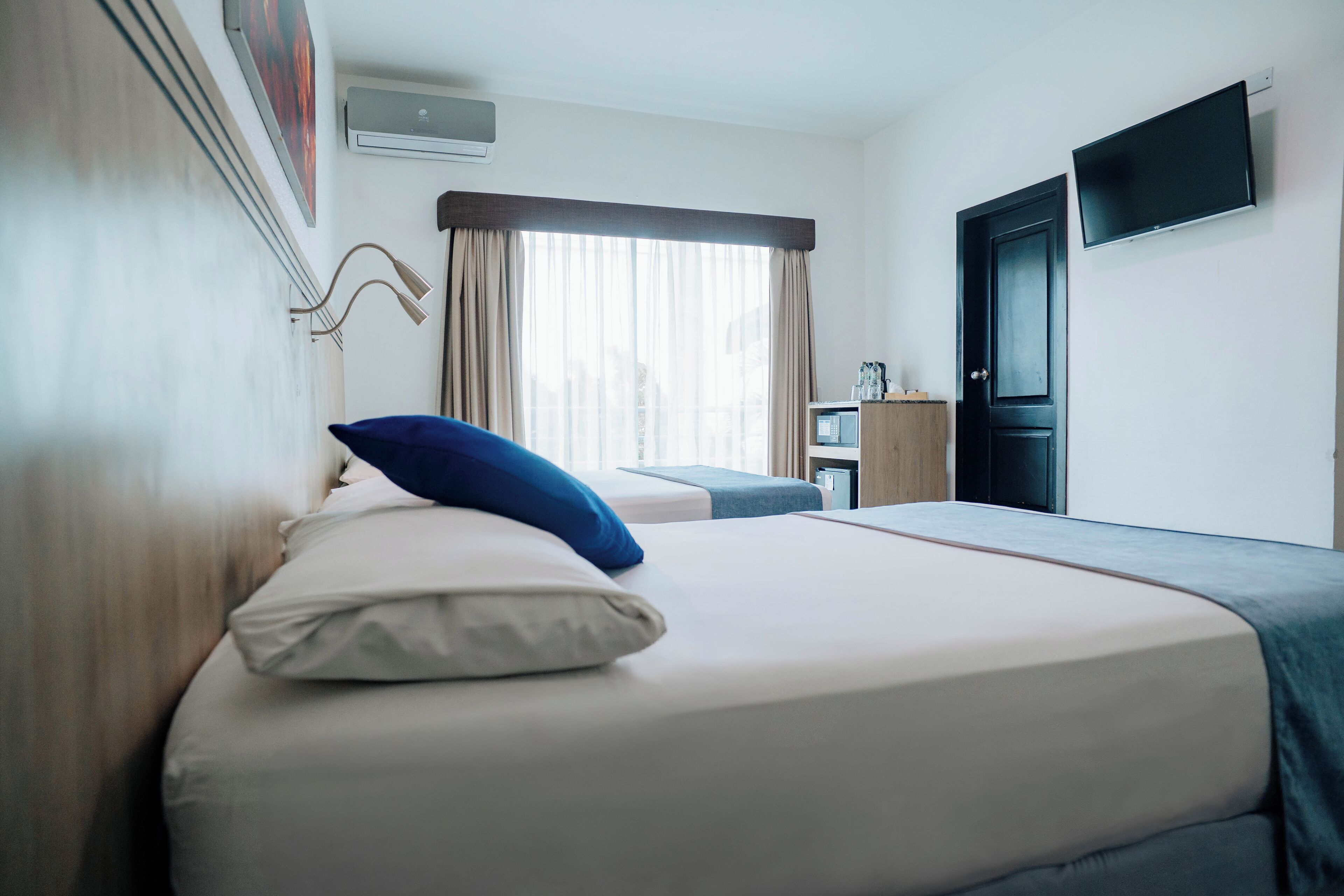 A hotel room with a bed, a desk, a television, and a window with curtains.