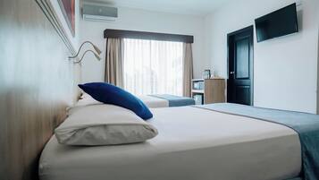 A hotel room with a bed, a desk, a television, and a window with curtains.