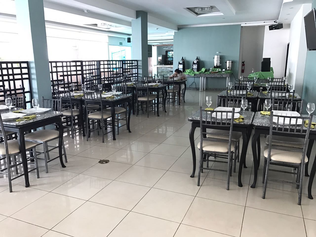 A restaurant with multiple tables and chairs, a tiled floor, and a kitchen area in the background.