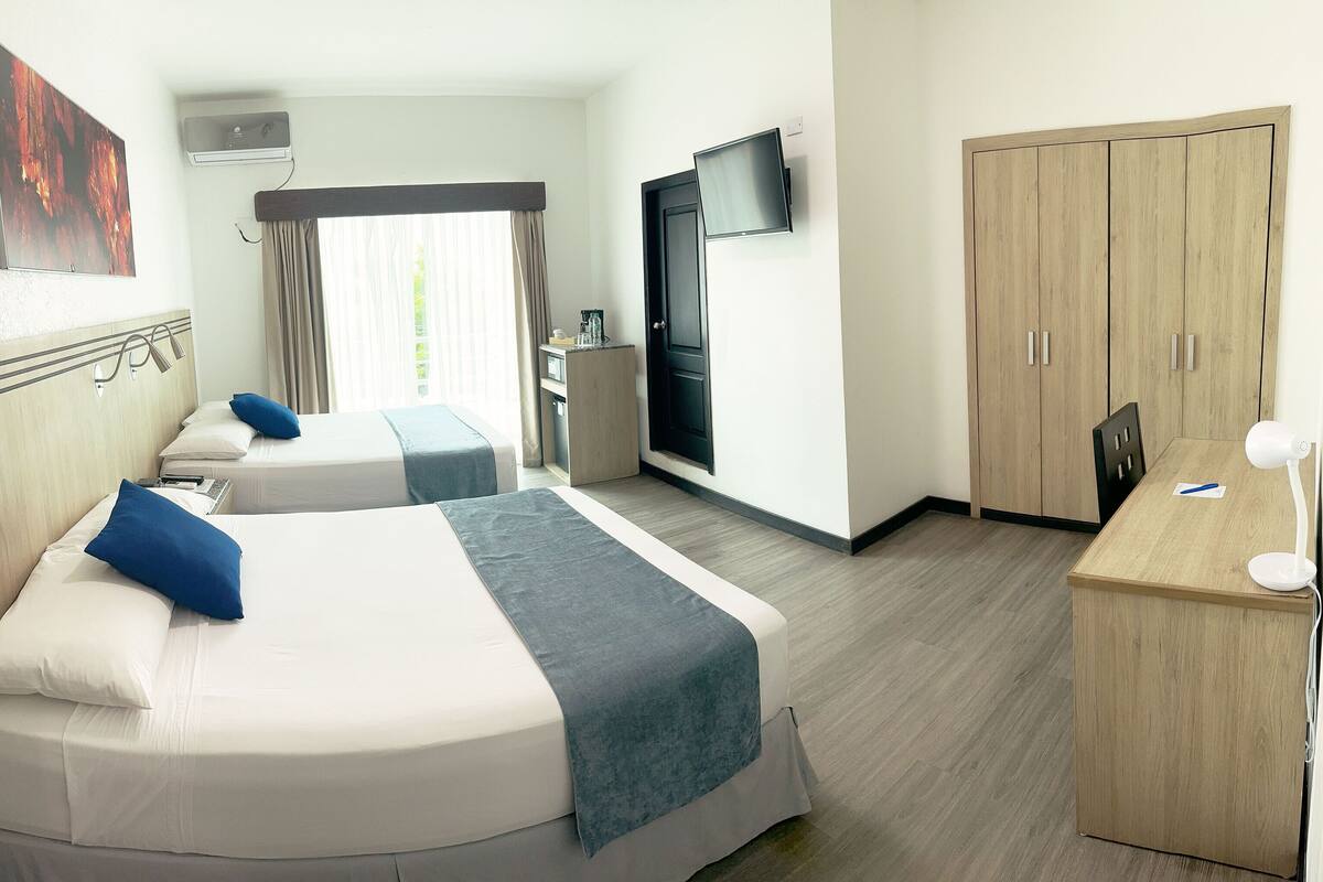 A hotel room with two beds, a desk, a wardrobe, and a TV.