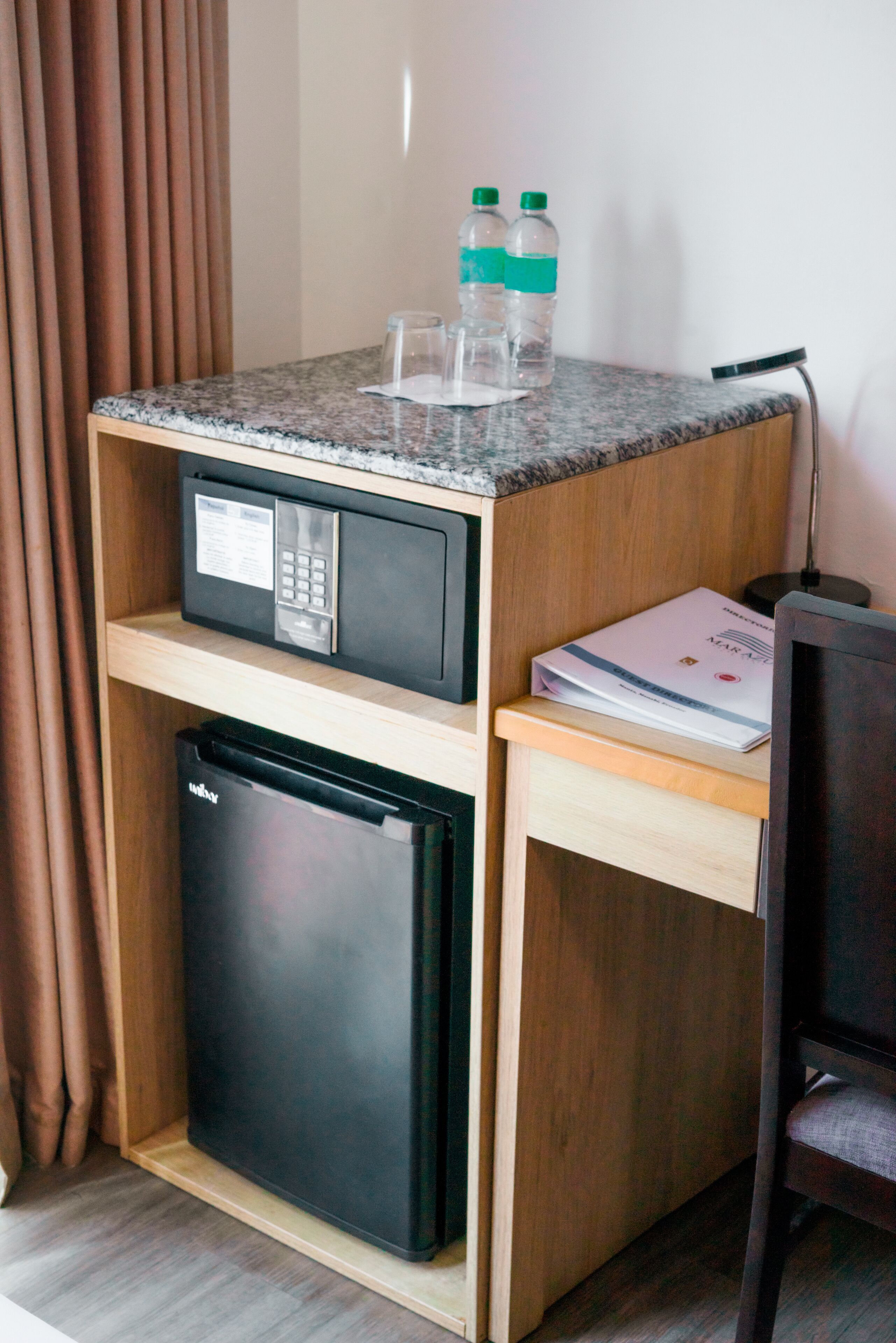 A compact kitchenette with a microwave, refrigerator, and countertop. There are two water bottles and a glass on the counter.