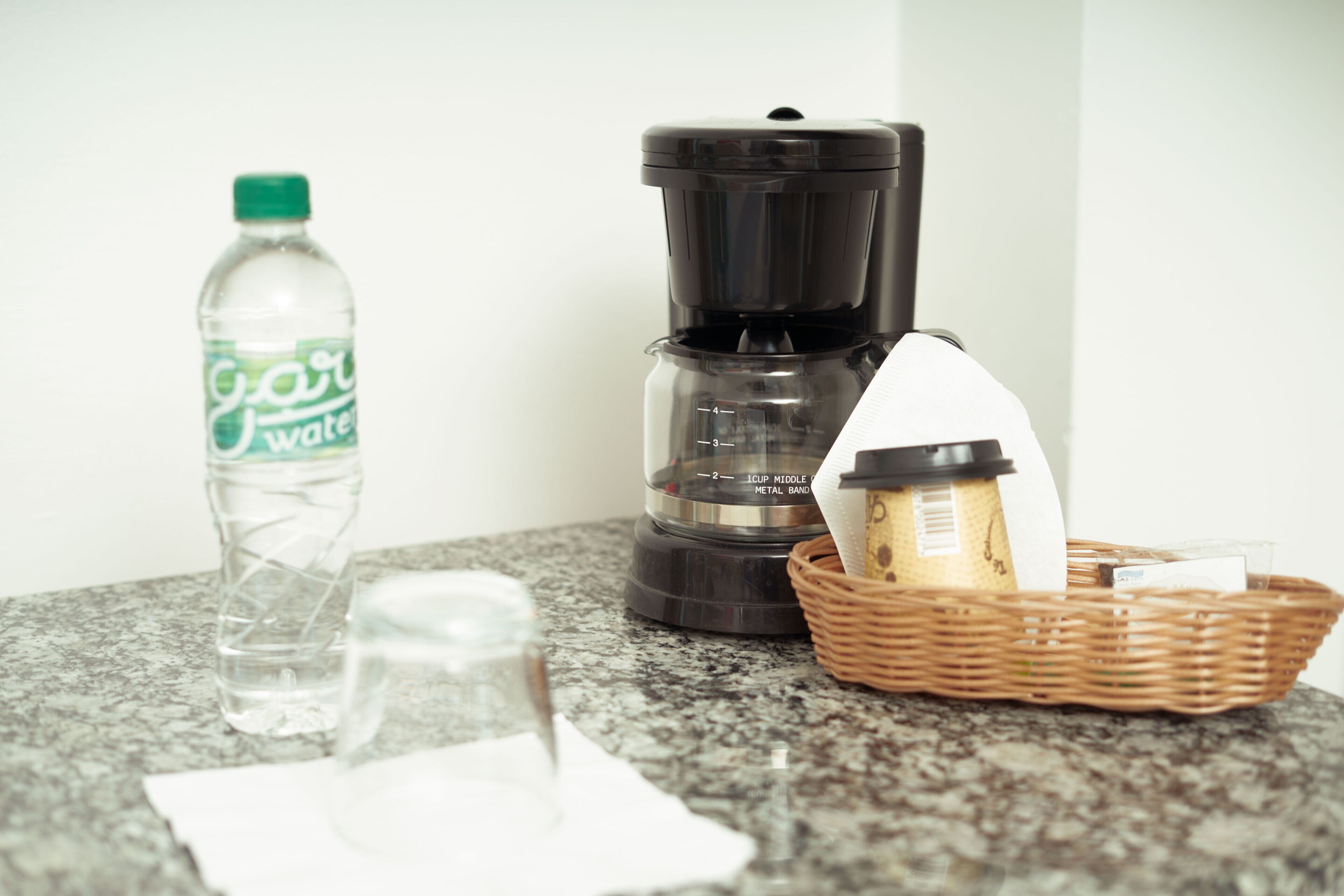 Eine Küchenarbeitsplatte mit einer Wasserflasche, einer Kaffeemaschine und einem Korb mit Brot und einer Kaffeetasse.