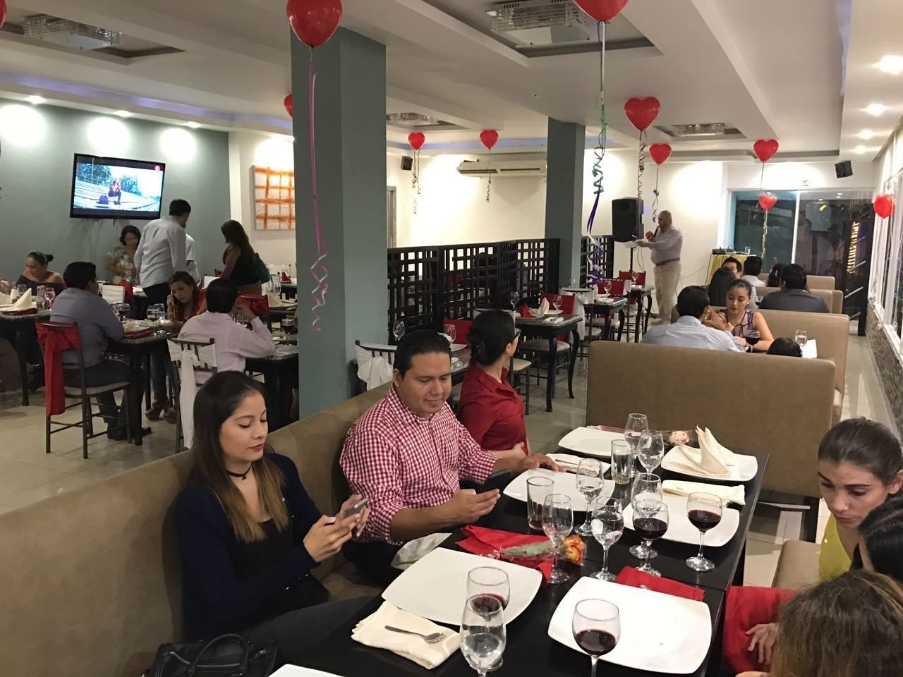 Un restaurante con mesas dispuestas para comer, una pantalla de televisión en la pared y globos rojos.