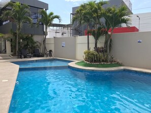A swimming pool with lounge chairs and palm trees, surrounded by buildings. - Hotel Mar Azul (Manta)