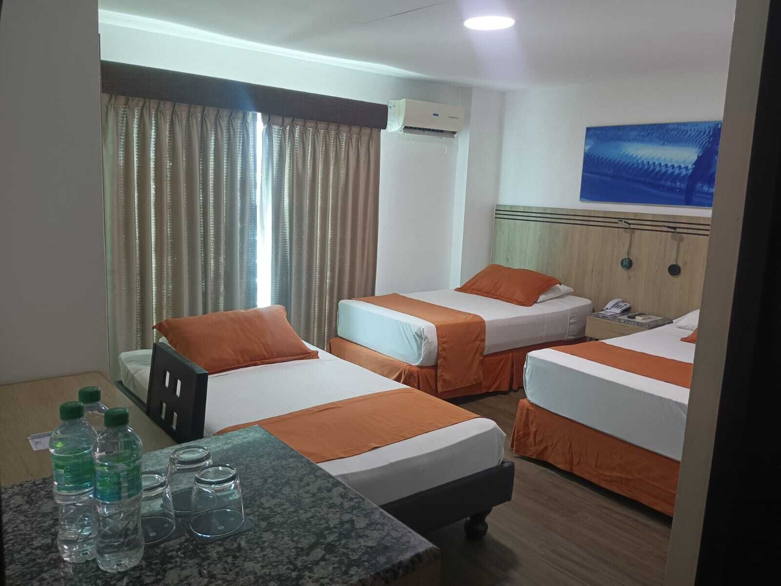 Una habitación de hotel con dos camas, una mesa con botellas de agua y un cuadro en la pared.