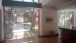 L’entrée d’un hôtel, avec une porte en verre, un sol carrelé et une poubelle.